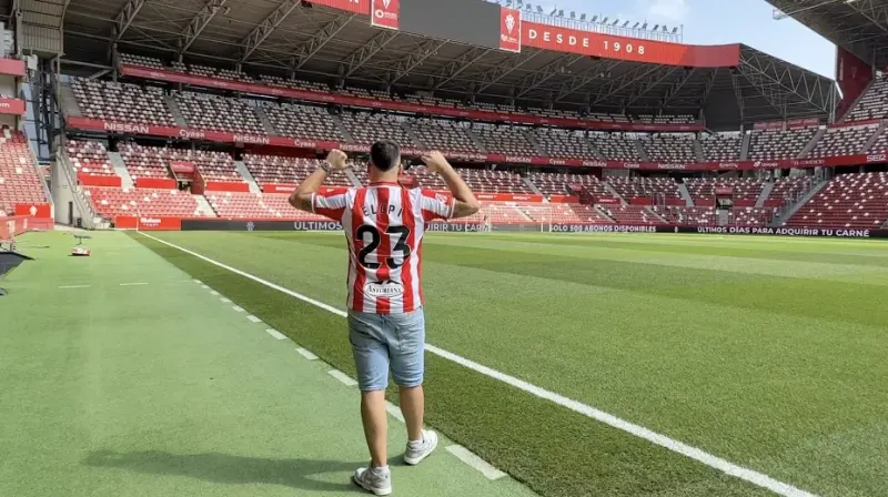 Elopi23 de espaldas sobre el césped de El Molinón con la camiseta del Sporting serigrafiada con ELOPI 23 y la grada vacía al fondo
