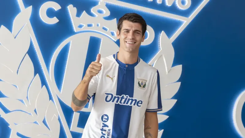 Álvaro Morata sonriente con la camiseta del CD Leganés y el pulgar arriba, delante del escudo del club