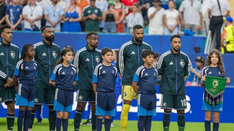 Jugadores de la selección de Arabia Saudí, con chándal verde, alineados junto a los niños de la mano antes de un partido del Mundial 2026