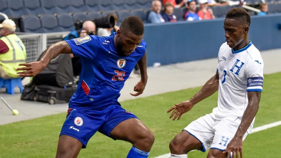 Duckens Nazon, con la camiseta azul de Haití, protege el balón ante un defensa de Honduras